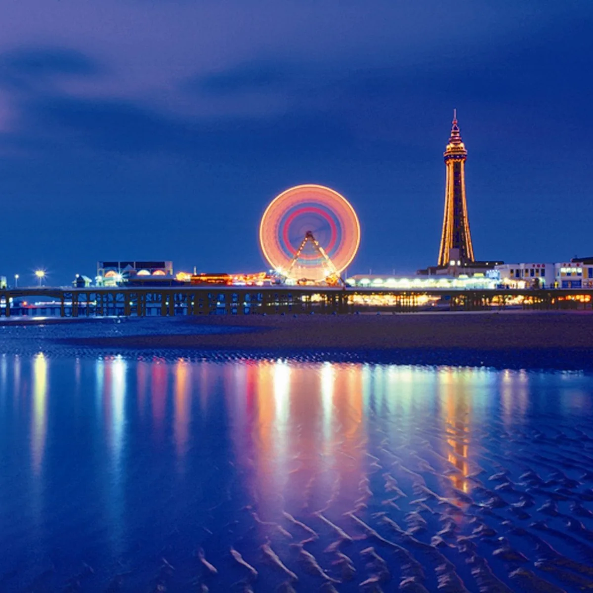 Blackpool Tower and Central Pier lights reflecting on the beach at night, England